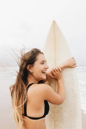 Creative Highlights Symbolfotos MR_BegonaVaello_YoungWomanSurf.jpg, PR_Tattoos_YoungWomanSurf.jpg Side view of positive young female athlete in swimsuit with flying hair and surfboard looking away on ocean beach, Property released Model Released LeoPastor_ID18073_543744_015 Copyright: xLeoxPastorx