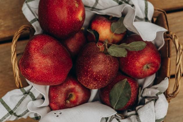 Top view of rustic basket filled with juicy, red apples, accented by green leaves and a striped cloth, presenting a fresh and organic scene. Model Released Ptashkimenko_ID26189_755652_004 Copyright: xx