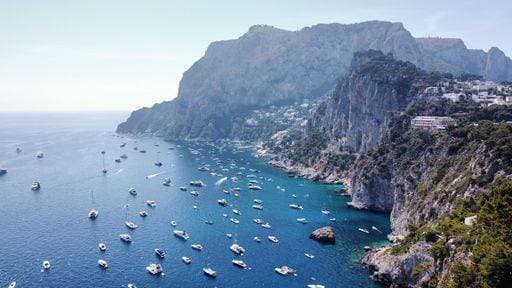 Aerial view of the stunning coastline of Capri, Italy, with numerous boats in the clear blue sea and rocky cliffs in the background. 25567409 RECORD DATE NOT STATED