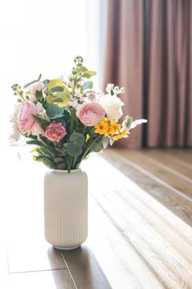 Ein Strauß aus Rosen, Ranunkeln und gelben Blüten ziert eine weiße, gerippte Vase, wobei rosa Vorhänge einen zarten und bezaubernden Hintergrund für das Blumenarrangement bilden A bouquet of roses, ranunculus, and yellow blossoms graces a white ribbed vase, with pink curtains providing a soft and enchanting backdrop to the floral arrangement Copyright: xZoonar.com AnnaxLuryex 22896416