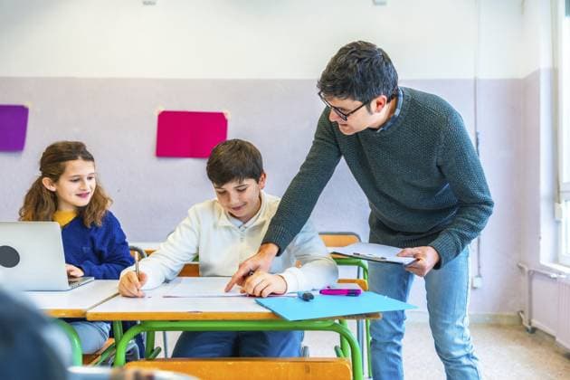 Lehrer, der den Schülern im Klassenzimmer hilft, Konzepte erklärt und Übungen korrigiert, während er eine unterstützende Lernumgebung fördert Teacher assisting students in the classroom, explaining concepts and correcting exercises while fostering a supportive learning environment Copyright: imageBROKER UnaixHuizi ibxuhu12678451.jpg ,model released, Symbolfoto ,property released