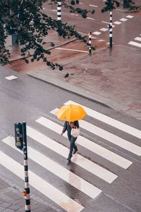IMAGO Creative, Jahreszeit Herbst in der Stadt A person with a yellow umbrella crossing a wet street on a rainy day, viewed from above, with zebra crossing and wet pavement visible. 28003922 RECORD DATE NOT STATED