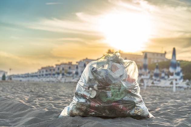 Italy - September 16, 2022: A filled garbage bag with plastic waste lies in the sand on a beach in Italy. The waste shows the environmental pollution and the problem of plastic waste in tourist coastal regions *** Ein gefüllter Müllsack mit Plastikabfällen liegt im Sand an einem Strand in Italien. Der Abfall zeigt die Umweltverschmutzung und das Problem von Plastikmüll in touristischen Küstenregionen