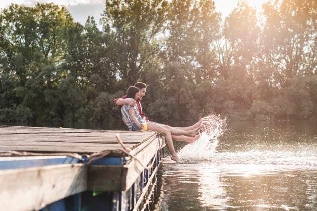 Happy young couple having a drink and splashing with water on jetty at a remote lake model released, Symbolfoto, UUF17938