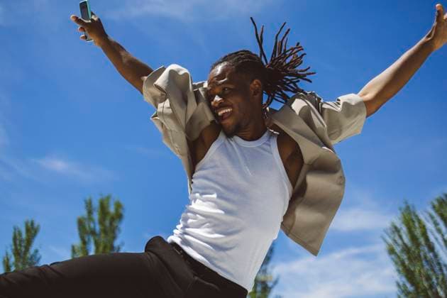 Cheerful young man holding smart phone and jumping under blue sky on sunny day model released, Symbolfoto, ALZF00972