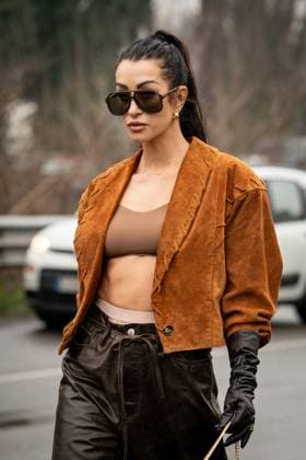 Street Style at Milan Fashion Week 2025 - Gucci in Milan, Italy on 25 February 2025 Street Style: A guest wears black Gucci sunglasses, gold earrings, silver necklace, light brown cropped suede jacket, dark brown bralette top, Gucci cream underwear, shiny black long leather gloves outside of the Gucci fashion show during the Milan Fashion Week Womenswear Fall Winter 2025 2026 in Milan, Italy on 25 February 2025., Credit:Stefano Costantino TTL Avalon Milan, Italy Copyright: xStefanoxCostantinoxTTLx xAvalonx 0968952624
