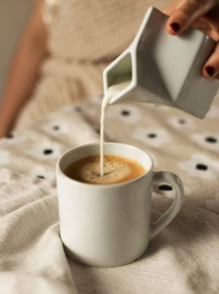 Woman pouring milk into mug of coffee Seattle, Washington, United States R_AAGC250225-1661726-01 ,model released, Symbolfoto