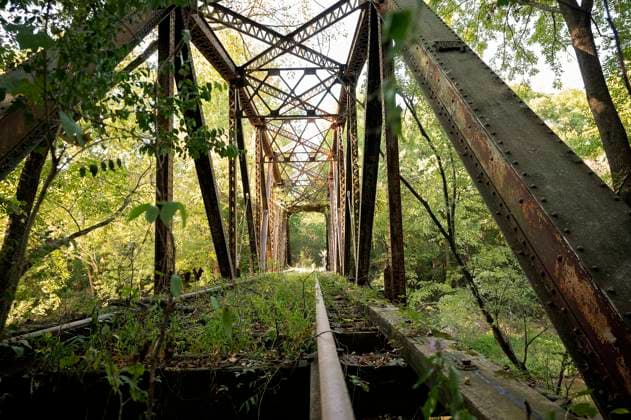 Overgrown abandoned railway bridge with rusty tracks and lush greenery Danville, Arkansas, United States R_JFXH250225-1661914-01