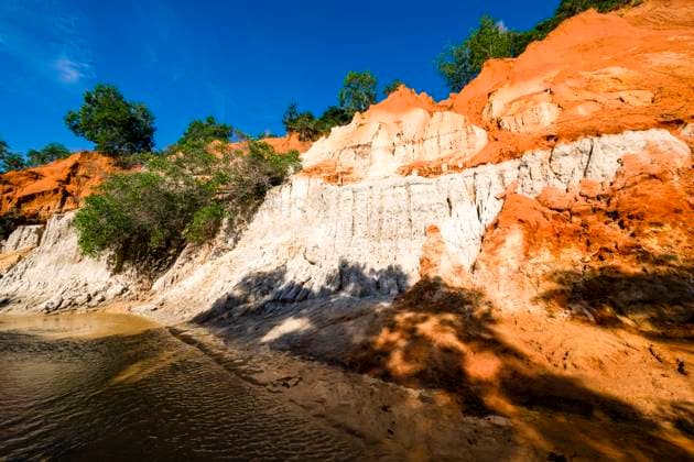 Orange and white coloured cliffs with small trees in the little canyon Fairy Stream, Suoi Tien, Suá»‘i TiÃªn near Mui Ne, MÅ i NÃ . Mui Ne Binh Thuan Province Vietnam FB_2024_4533
