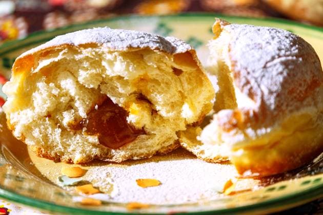 mit Marillenmarmelade gefüllter Faschingskrapfen mit Puderzucker, in der Mitte zerteilt, Keramikteller weiß-grün melliert, gemusterte Tischdecke, Konfetti *** Carnival doughnut filled with apricot jam and powdered sugar, cut in the middle, ceramic plate white green mottled, patterned tablecloth, confetti