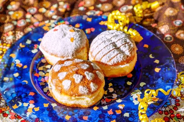 bunte gefüllte Faschingskrapfen (Vanille, Marillenmarmelade, Hagebuttenmarmelade), Glasteller blau, gemusterte Tischdecke, Konfetti, gelbe Luftschlangen *** colorful filled carnival doughnuts vanilla, apricot jam, rose hip jam, blue glass plate, patterned tablecloth, confetti, yellow streamers