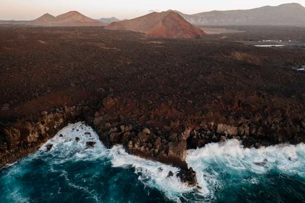 Captivating aerial shot showcasing the rugged coastline and volcanic terrain of Los Hervideros, Lanzarote, with waves crashing along the shore at sunset. Model Released DavidJerez_ID26518_765663_032 Copyright: xDavidxJerezx