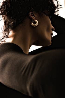 Creative Highlights Symbolfotos A woman in a dark outfit poses with her face turned away, highlighting a large, textured earring. The lighting creates a dramatic shadow effect on her skin. Model Released FranRuiz_ID26430_762524_012 Copyright: xFranxRuizx RECORD DATE NOT STATED