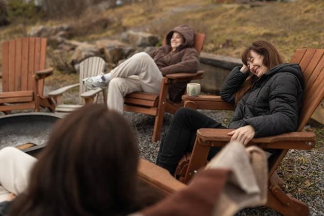 Three female friends enjoy a relaxing time together outdoors, sitting in wooden chairs and laughing around a fire pit. They are dressed warmly and the setting is a natural, wooded area. Model Released Ptashkimenko_ID26860_775346_005 Copyright: xPtashkimenkox