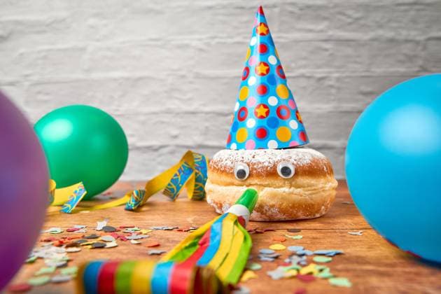 Germany - February 28, 2025: A Berliner with wiggly eyes, a party hat and a horn for a mouth, surrounded by carnival decorations, balloons and streamers *** Ein Berliner mit Wackelaugen, Partyhut und einer Tröte als Mund, umgeben von Faschingsdekoration, Luftballons und Luftschlangen
