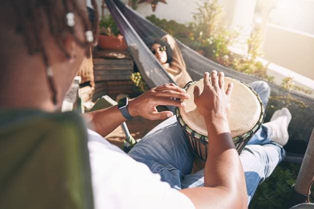 Friends, relax and playing drums for fun, outdoor balcony and musician practice with instrument. Bongo, music hobby and chilling together on weekend for peace, people and hammock for artistic bonding. model released property released Copyright: xROWANxJORDAN(PTY)LTDx