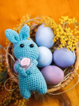 Gestrickter Osterhase mit einer Blume in den Pfoten, bunt bemalte pastellfarbene Eier in einem Weidenkorb Knitted Easter bunny with a flower in its paws, painted colorful pastel eggs in a wicker basket Copyright: xZoonar.com PavelxMarysx 22945004