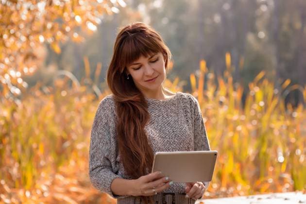 Porträt einer glücklichen, schönen Frau mit langen braunen Haaren, die in einem herbstlichen Park sitzt Portrait of a happy, beautiful woman with long brown hair, sitting in an autumn park with yellow foliage, holding a digital tablet in her hands. Remote work, education concept. Copy space ,model released, Symbolfoto Copyright: xZoonar.com NatashaxZakharovax 22937729 ,model released, Symbolfoto ,property released