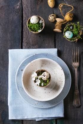 Colorful Easter quail eggs Table setting decor colorful Easter quail eggs with spring cherry flowers, moss in garden pots, empty plates, cutlery over old wood background. Dark rustic style. Top view with copy space. Copyright: xZoonar.com NatashaxBreenx 22981063