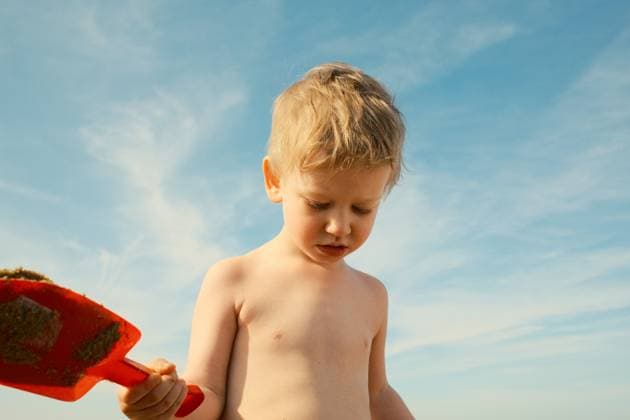 Creative Highlights Symbolfotos Blond boy holding red shovel with sand looking down at the beach The Hague, South Holland, Netherlands CR_OSBJ250212-1524851-01 ,model released, Symbolfoto