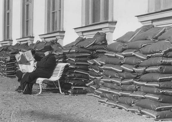 In den 1940er Jahren. Ein älteres Ehepaar sitzt auf einer Bank und liest eine Zeitung vor einem Gebäude, in dem sich vor den Kellerfenstern Säcke mit Sand aufgetürmt haben. Dies geschah, um das Gebäude und die darin befindlichen Personen im Falle eines Bombenangriffs zu schützen. Das Bild wurde am 12. April 1940 während des Zweiten Weltkriegs aufgenommen In the 1940s. An elderly couple is seen sitting on a bench reading a newspaper in front of a building with sacks of sands piled up in front of the basement windows. This was done to protect the building and any people inside if an airattack with bombs would happen. The picture taken 12 april 1940 during world war 2 Copyright: imageBROKER Sjoberg ibljsj12852882.jpg