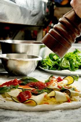 Cropped unrecognizable person seasons an uncooked pizza laden with fresh vegetables and cheese, enhancing the flavors before baking. Model Released DondykRiga_ID26863_775432_022 Copyright: xDondykxRigax RECORD DATE NOT STATED