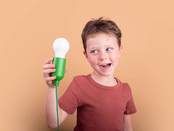 Creative Highlights Symbolfotos A cheerful child in a red shirt holds a green light bulb, set against a peach background. The image radiates innovation and youthful curiosity. Model Released HodeiUnzueta_ID27398_786278_007 Copyright: xHodeixUnzuetax