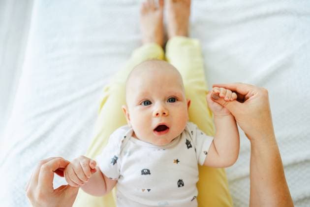 Creative Highlights Symbolfotos A baby in a patterned onesie lies on a mother lap, holding their hands. The setting is cozy and bright, capturing a moment of bonding and tenderness. Model Released JenyKulikova_ID27010_779550_009 Copyright: xJenyxKulikovax