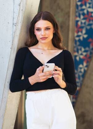 Creative Highlights Symbolfotos Young woman in a black top and white pants holds a smartphone, leaning against an architectural wall with geometric patterns, in a stylish urban setting. Model Released Jultud_ID25621_739943_004 Copyright: xJultudx