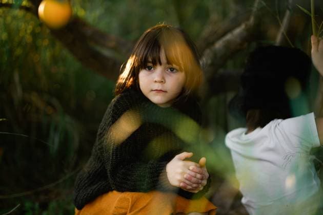MR_ID26943_20137_LeoBosquetLaguna.jpg, MR_ID26943_20138_MayaBosquetCarli.jpg A young girl with deep eyes sits in a wooded area, hands clasped, bathed in soft golden light. A boy, partially visible, faces away, adding mystery and storytelling to this quiet outdoor moment. Model Released MagdalenaCarli_ID26943_777384_001 Copyright: xMagdalenaxCarlix RECORD DATE NOT STATED