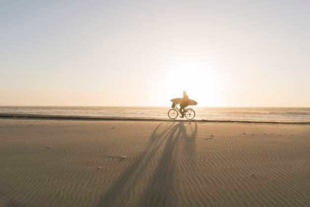Creative Highlights Symbolfotos Surfer riding a bicycle during the sunset in the beach, Costa Nova, Portugal model released, Symbolfoto, AHSF01043
