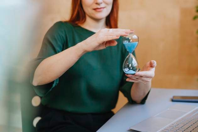 Creative Highlights Symbolfotos Woman in green shirt holding an hourglass at a table with a laptop model released, Symbolfoto property released, YTF03562