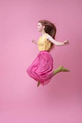 Creative Highlights Symbolfotos Red-haired girl jumping in a studio with a pink background wearing a long skirt and green tights model released, Symbolfoto, VRAF01119