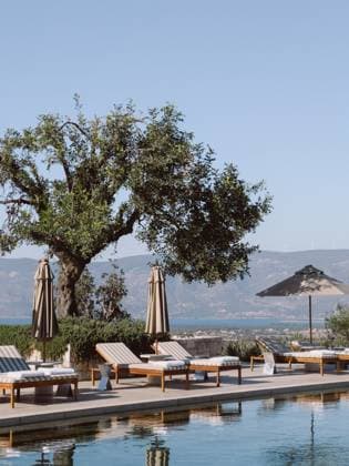 Sun loungers and sun umbrellas stand by the pool against the backdrop of the mountains. Hotel Amanzoe, Greece. High quality photo , 56485230.jpg, travel, tourism, sun, loungers, umbrellas, stand, pool, mountains, hotel, amanzoe, greece, green, tree, mattress, pillows, reflection, blue, sky, luxury, resort, beach, club, wealth, leisure, close up RECORD DATE NOT STATED