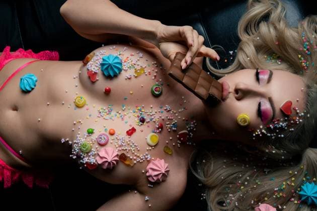 Creative Highlights Symbolfotos Frau mit Körperkunst und bunter Süßigkeiten-Dekoration, die Schokolade genießt A woman lies on a dark surface, adorned with body art and vibrant candy decorations while savoring a piece of chocolate. ,model released, Symbolfoto Copyright: xZoonar.com AndreyxGuryanovx 23127692 ,model released, Symbolfoto ,property released