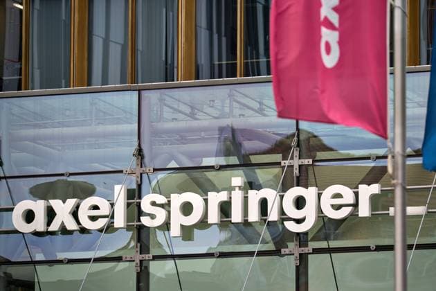 Axel-Springer-Schriftzug am Glasfassaden-Eingang des Verlagshauses in Berlin mit reflektierten Strukturen und wehenden Firmenflaggen