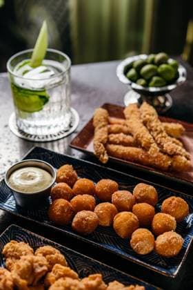 IMAGO Creative, Food, Tapas A variety of tapas featuring fried shrimp and golden-brown bites, complemented by a refreshing cocktail with lime garnishes. Perfect for a cozy dining experience. Model Released Andrerako_ID26660_769220_023 Copyright: xAndrerakox RECORD DATE NOT STATED