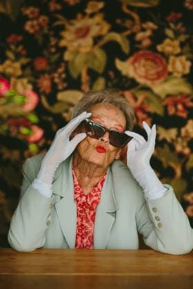Creative Highlights Symbolfotos Chic grandma poses playfully in a studio setting, wearing sunglasses and gloves against a floral backdrop. Her lively expression and fashion sense exude confidence and charm. Model Released CamilleGirard_ID26984_778919_022 Copyright: xCamillexGirardx RECORD DATE NOT STATED