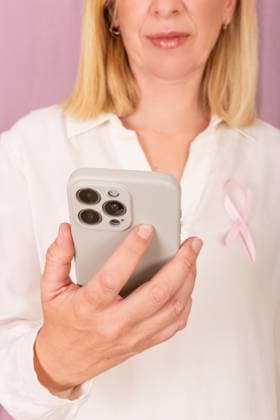 MR_ID27730_20456_RuthAlejo.jpg A woman wearing a pink ribbon symbolizes breast cancer awareness. She is looking at her smartphone, promoting vigilance and support for cancer prevention. Model Released GemaAlejo_ID27730_796141_009 Copyright: xGemaxAlejox