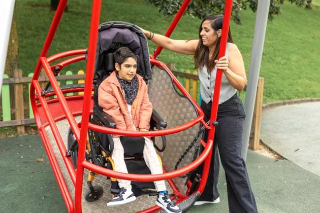 A child with cerebral palsy sits in a specialized wheelchair accessible swing at a playground, while a mother helps push. The playground is designed for fun and inclusivity. Model Released JuanAizpuru_ID26728_771495_003 Copyright: xJuanxAizpurux RECORD DATE NOT STATED