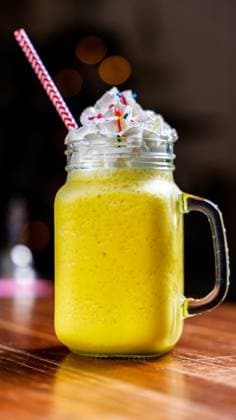 A vibrant mango smoothie topped with creamy whipped cream and colorful sprinkles, served in a mason jar with a striped straw on a wooden cafe table. Perfect for summer vibes. Model Released LeoTenorio_ID27358_784894_019 Copyright: xLeoxTenoriox RECORD DATE NOT STATED