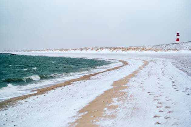 Snow-covered beach with waves crashing and a distant lighthouse on the horizon. Sylt, Germany Sylt Germany bola08303 Copyright: xConnectxImagesx
