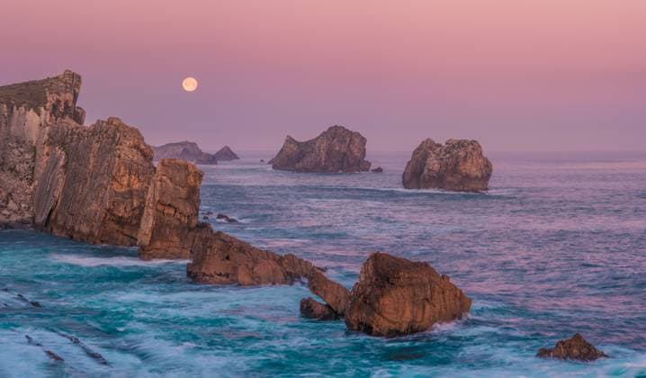 A serene view of rugged sea stacks and cliffs bathed in soft dawn light at Arnia Beach, Costa Quebrada, with the full moon glowing over the tranquil Atlantic horizon Model Released FranciscoCarrodeguas_ID26764_772492_001 Copyright: xFranciscoxCarrodeguasx RECORD DATE NOT STATED