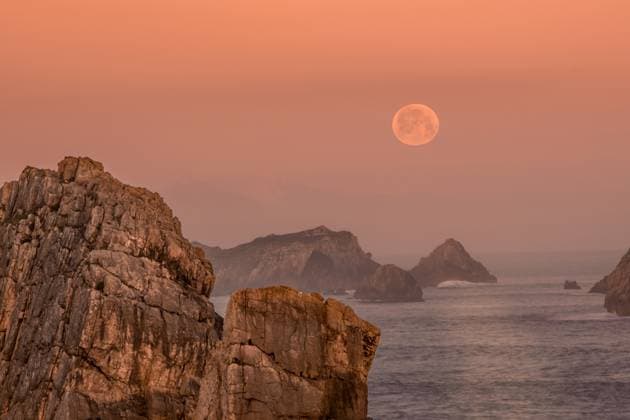 The full moon hovers above jagged rock formations along the Atlantic coast of Arnia Beach, Costa Quebrada, as the sky glows with soft sunrise hues in Cantabria Model Released FranciscoCarrodeguas_ID26764_772498_004 Copyright: xFranciscoxCarrodeguasx RECORD DATE NOT STATED
