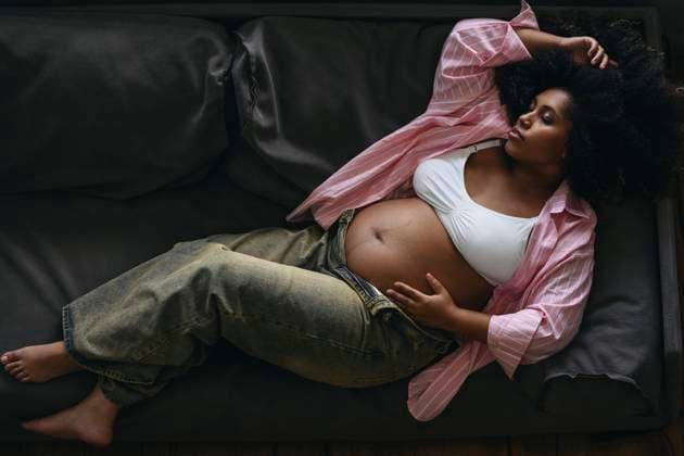 Creative Highlights Symbolfotos Pregnant woman with closed eyes in pink stripe shirt lying on sofa model released, Symbolfoto property released, EYAF03383