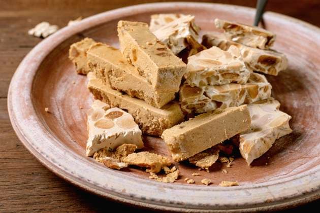 Spanish dessert classic turron Traditional Spanish dessert classic soft orange turron and crunchy almond turron, cut into pieces on rustic clay plate with fork. Wooden table, top view. Copyright: xNatashaxBreenx NB070325-12