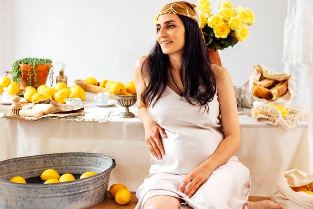 Creative Highlights Symbolfotos Eine schwangere Frau in einem Satinkleid sitzt an einem Tisch mit Zitronen, Küchenutensilien und Brot. Die Frau lächelt und berührt sanft ihren Bauch. Pregnant woman in a satin dress sits beside table with lemons, kitchen utensils and bread. Lady smiles and gently touches her belly. Joyful future mother with headscarf. Rustic vintage interior (License=RF) ,model released, Symbolfoto Copyright: xZoonar.com DashaxPetrenkox 23320908 ,model released, Symbolfoto ,property released