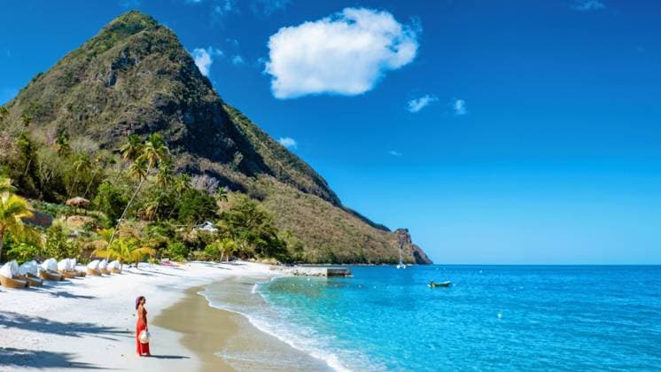 St Lucia Karibik, Frau im Urlaub auf der tropischen Insel Saint Lucia An Asian woman in a flowing red dress strolls along the golden sands of Saint Lucia, embraced by the tranquil turquoise waters and lush green mountains under a clear blue sky. (License=RF) ,model released, Symbolfoto Copyright: xZoonar.com FokkexBaarssenx 23346029 ,model released, Symbolfoto ,property released
