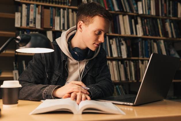 Männlicher Student in der Bibliothek mit Blick auf den Laptop. Junger Mann sitzt am Schreibtisch und bereitet Prüfungen am Abend vor. Male student in library looking at laptop. Young man sitting at desk preparing exams at evening. (License=RF) ,model released, Symbolfoto Copyright: xZoonar.com ArtemxVarnitsinx 23348611 ,model released, Symbolfoto ,property released