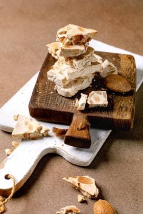 Spanischer Dessert-Klassiker Turron Traditional Spanish dessert classic crunchy turron with almonds, broken into pieces on wooden serving board. Beige textured background. (License=RF) Copyright: xZoonar.com NATASHAxBREENx 23371761